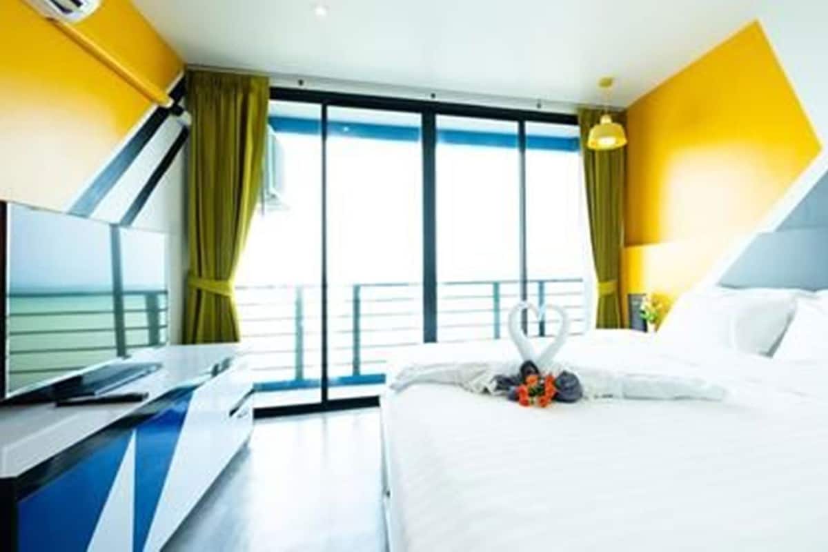 Une chambre d’hôtel équipée d’un lit, d’un bureau, d’une télévision et offrant une vue sur la mer grâce à de grandes fenêtres.