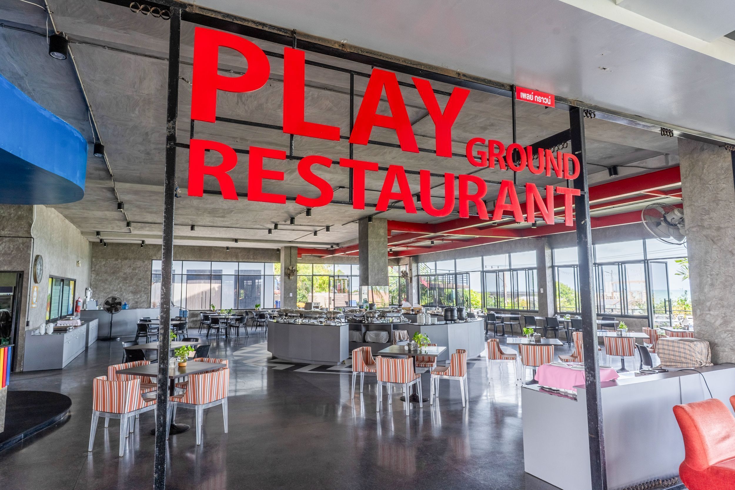 Ein geräumiger Innenbereich mit einem großen Schild, auf dem 'PLAY GROUND RESTAURANT' steht, und mehreren Sitzbereichen inklusive Tischen und Stühlen.