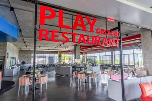 Un espacio interior amplio con un letrero grande que dice 'PLAY GROUND RESTAURANT' y varias zonas de estar con mesas y sillas.