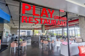Un espacio interior amplio con un letrero grande que dice 'PLAY GROUND RESTAURANT' y varias zonas de estar con mesas y sillas.