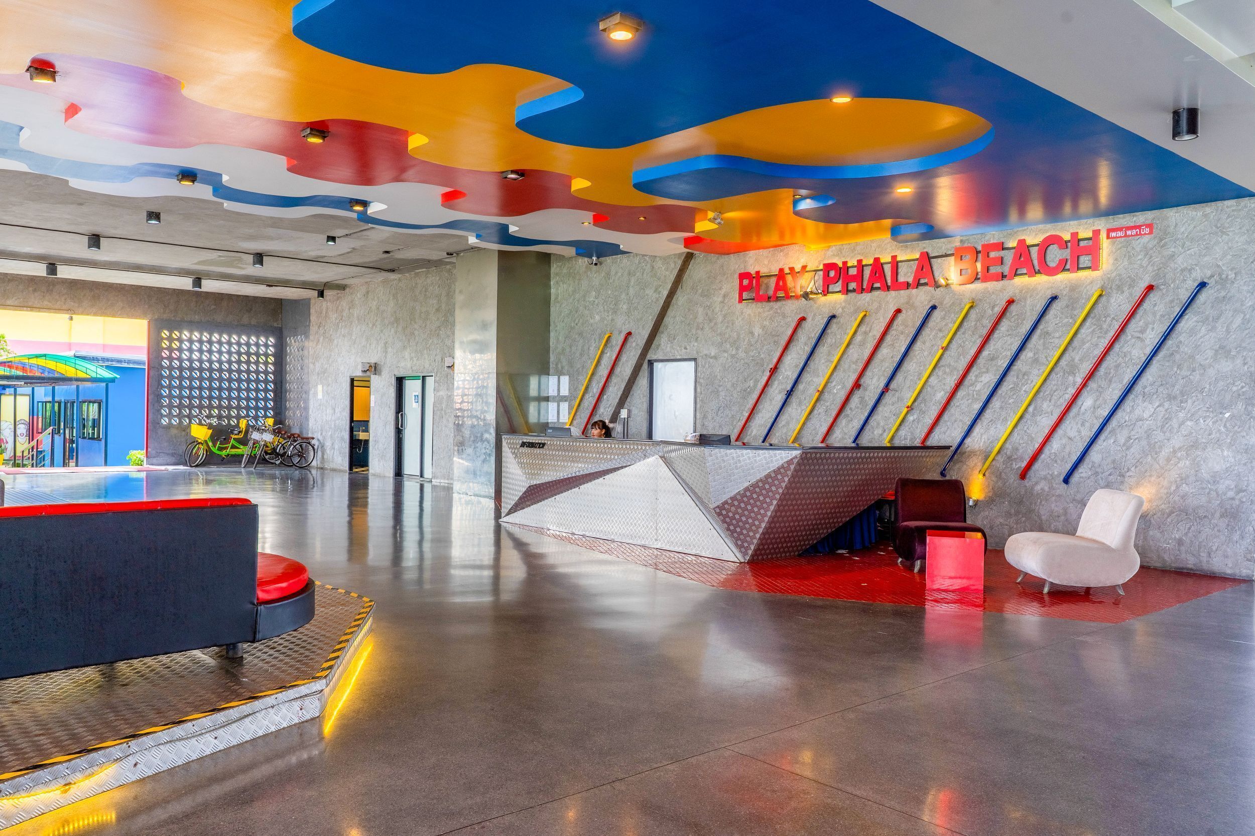 A modern reception area with a colorful ceiling, a sign reading 'PLAYPHALA BEACH', and a reception desk.
