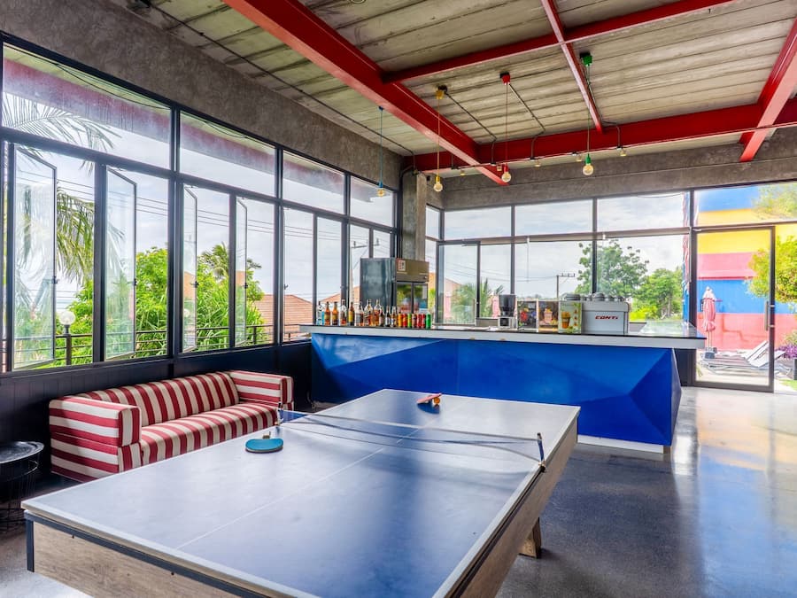 A spacious room with a ping pong table, a bar area with various bottles, and large windows offering a view of the outside.