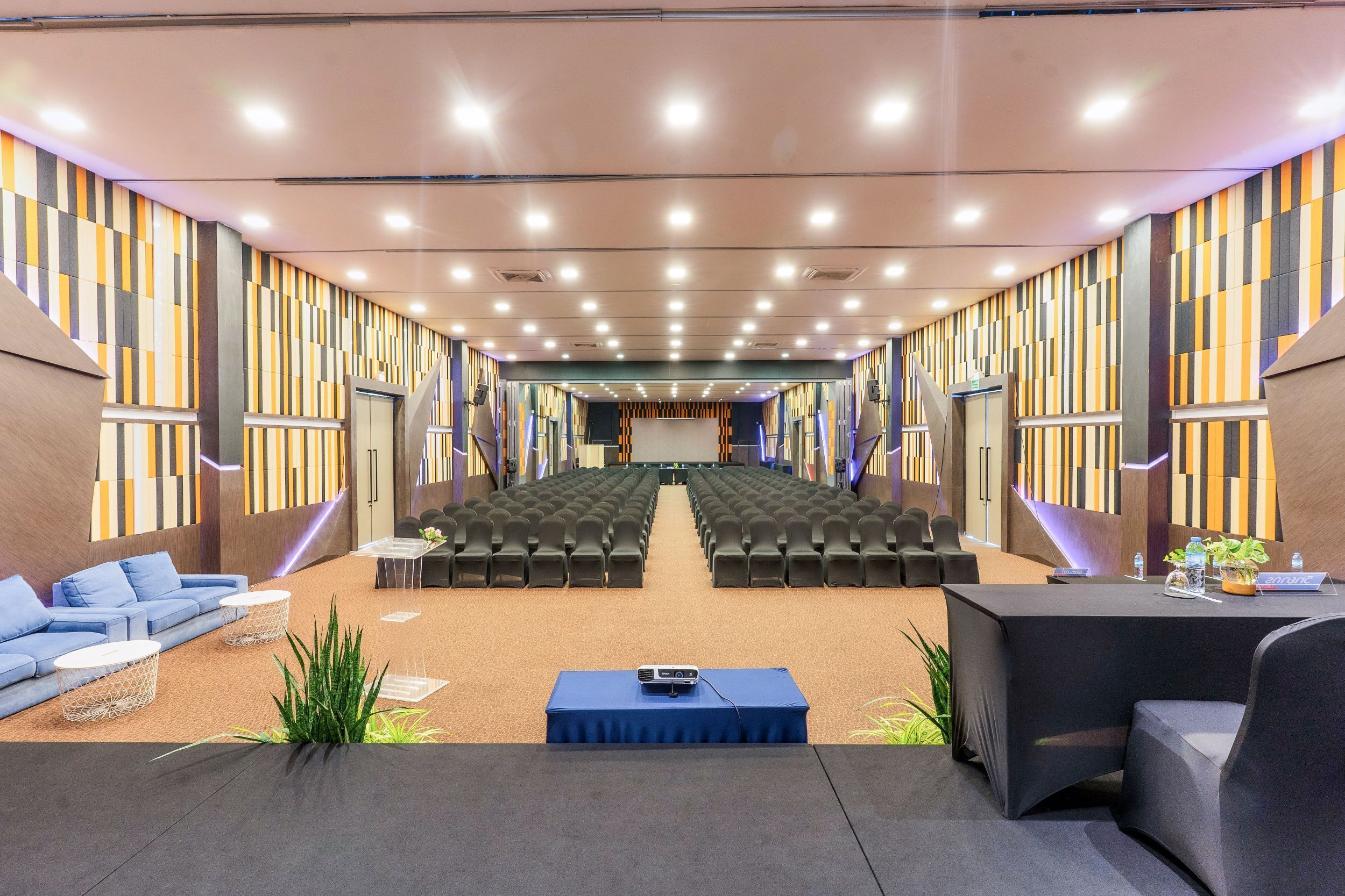 A conference room with rows of chairs, a stage, and a seating area with sofas and tables.