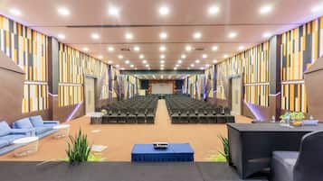 A conference room with rows of chairs, a stage, and a seating area with sofas and tables.