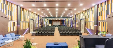 Un salón de conferencias con filas de sillas, un escenario y una zona de estar con sofás y mesas.