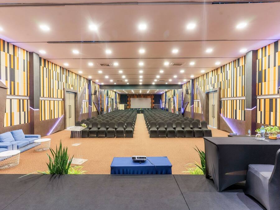 A conference room with rows of chairs, a stage, and a seating area with sofas and tables.