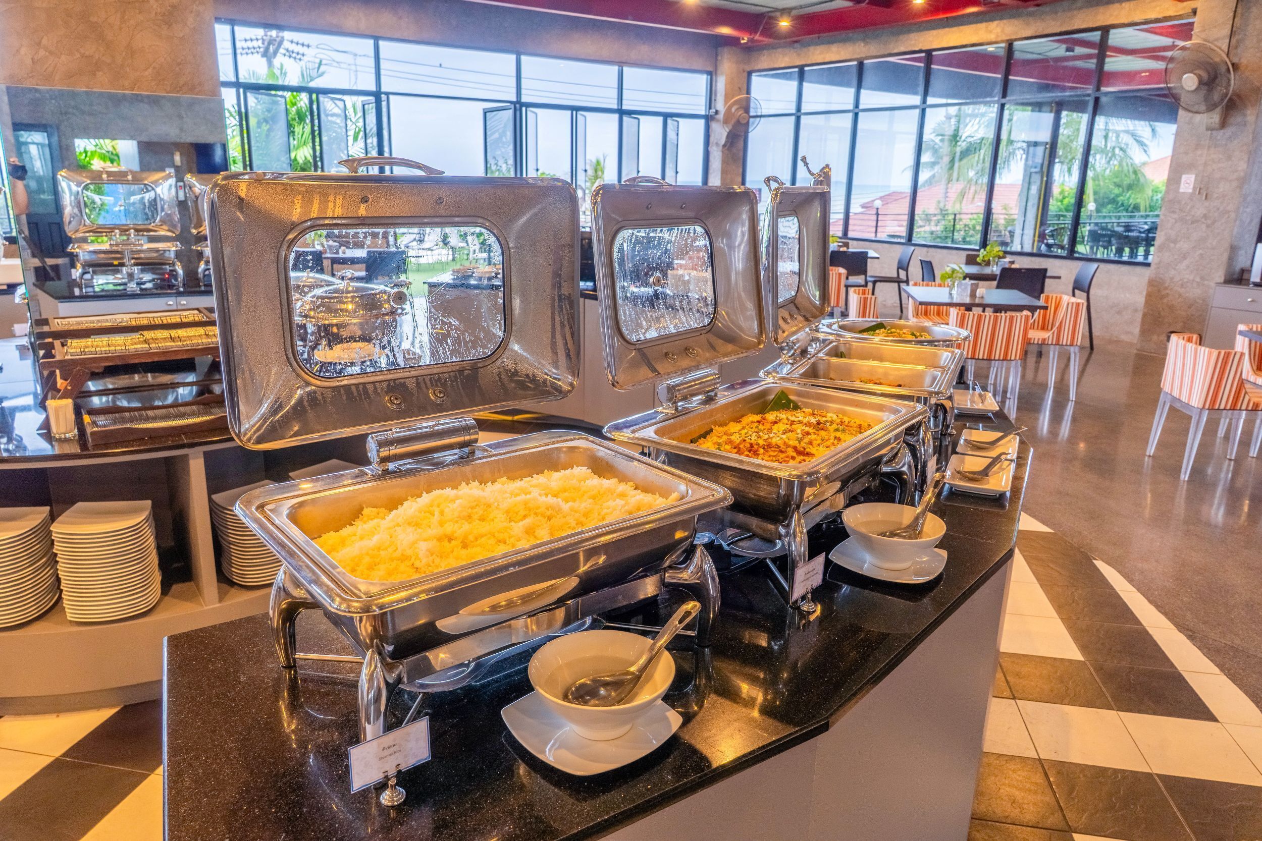 Disposición de bufé con varias estaciones de servicio, incluyendo una estación de arroz y un plato con guarnición verde.