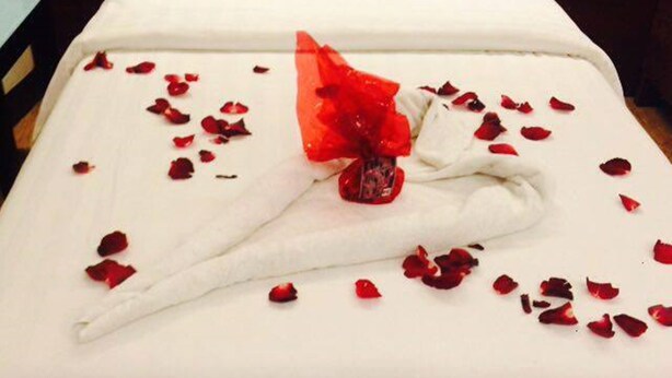 A neatly made bed with white linens, a red rose bouquet, and scattered rose petals. - Lindi Hotel Baguio (Baguio)