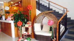 A reception area with a clock, a counter, and a wicker sofa with a cushion. - Lindi Hotel Baguio (Baguio)
