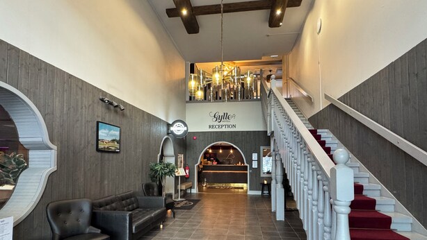 Zona de recepción de un hotel con escalera, mostrador y área de estar.