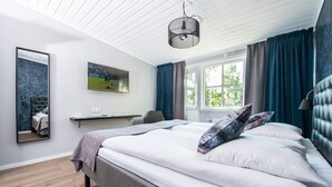 Un dormitorio moderno con una cama grande, un televisor montado, un escritorio y una ventana con cortinas.