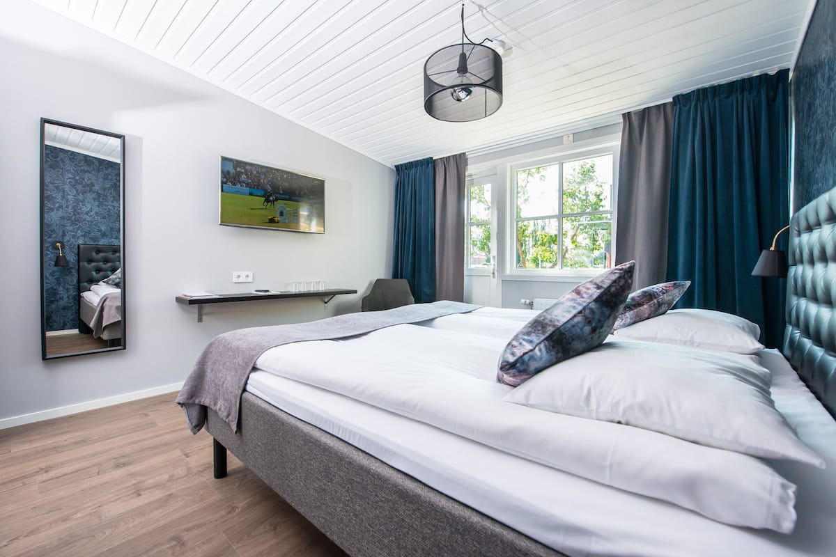 Une chambre moderne avec un grand lit, un téléviseur fixé au mur, un bureau et une fenêtre avec des rideaux.