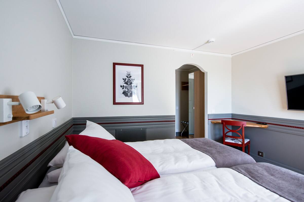 Une chambre d’hôtel avec un lit, une chaise rouge, un téléviseur et un tableau encadré au mur.