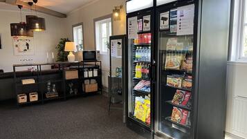 Eine Hotelhalle mit einer Selbstbedienungsgetränkestation, einer Sitzecke inklusive Sofa und Tisch sowie einem mit Snacks gefüllten Kühlschrank.
