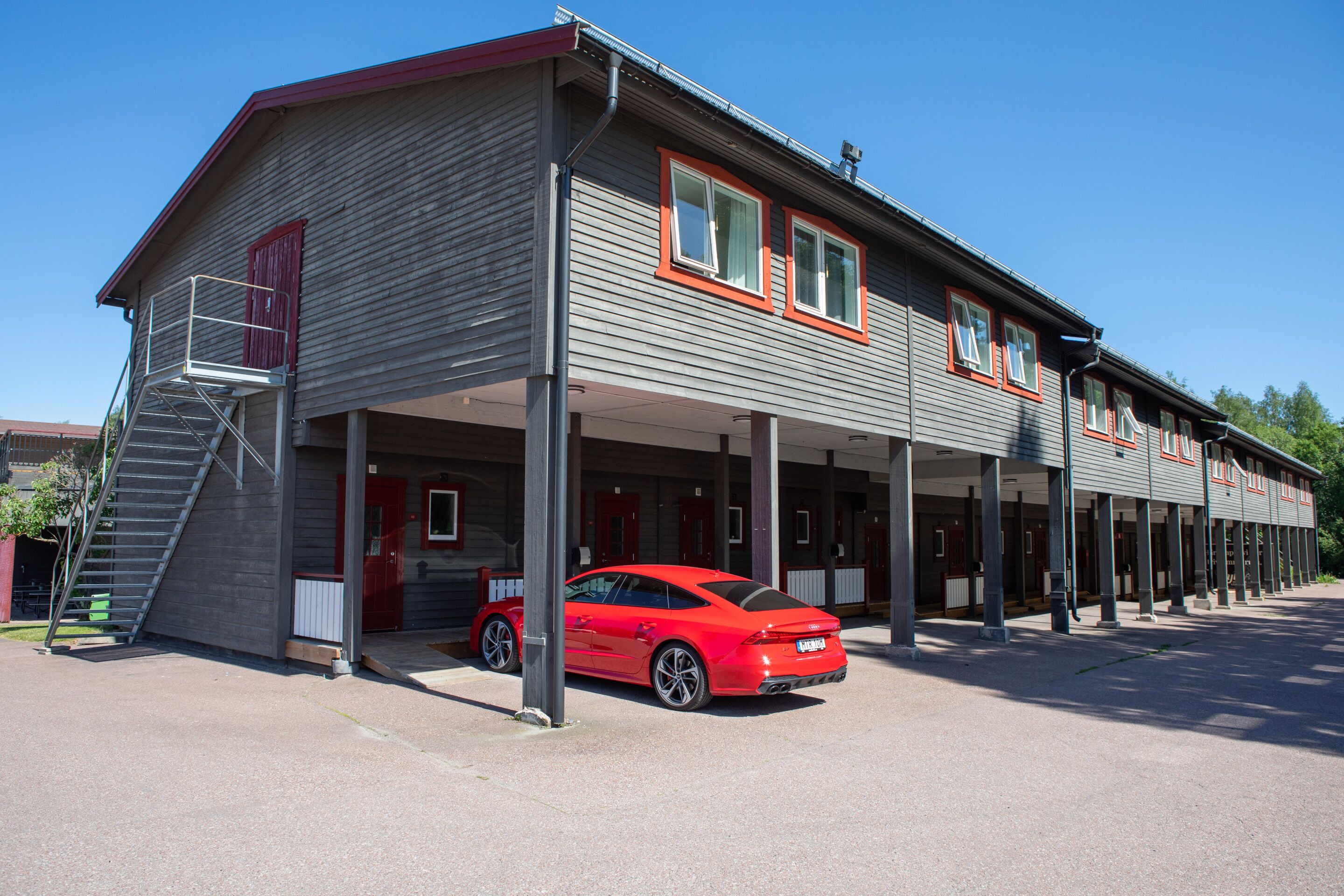 A two-story building with a covered parking area and a red sports car parked in front.