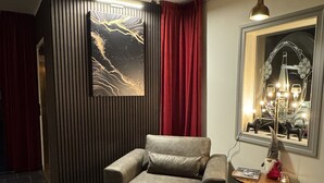 Una sala de estar moderna con un sofá gris, una cortina roja, una obra de arte colgada en la pared, una mesita con un objeto decorativo y una lámpara colgante.