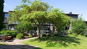 Un patio con mobiliario exterior, un árbol y un edificio al fondo.