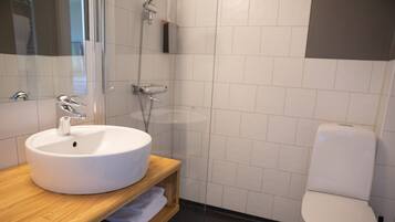 Un bany modern amb un lavabo blanc, un armari de tocador de fusta, una cabina de dutxa de vidre i un vàter blanc.