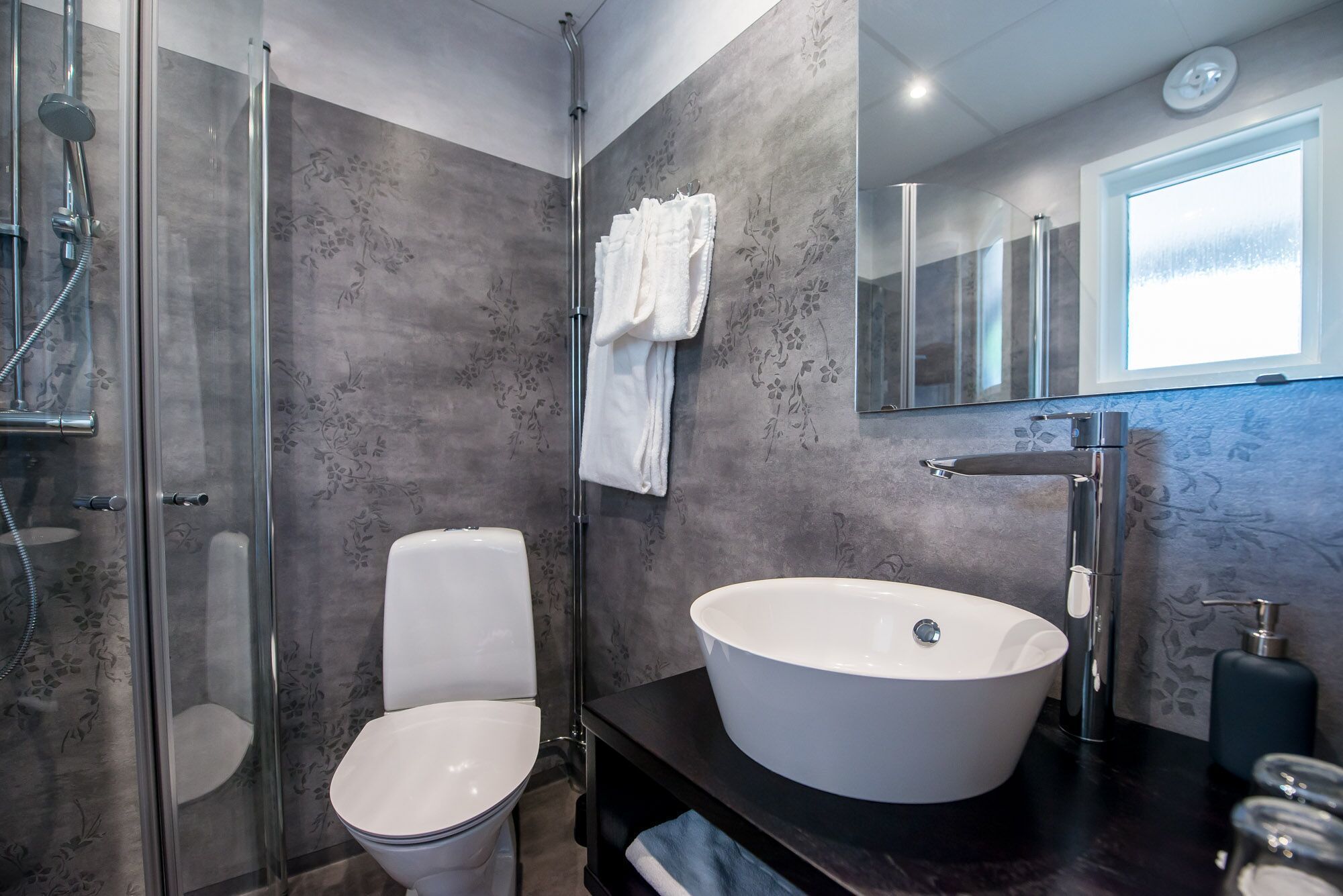 Une salle de bain moderne avec une douche à parois de verre, des toilettes, un grand lavabo sur pied et un miroir au-dessus du lavabo.