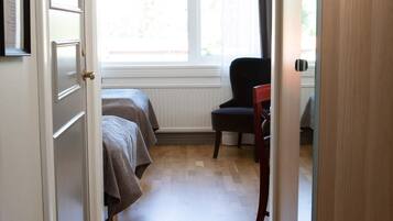 A narrow hallway leading to a bedroom with a window, a chair, and a bed.