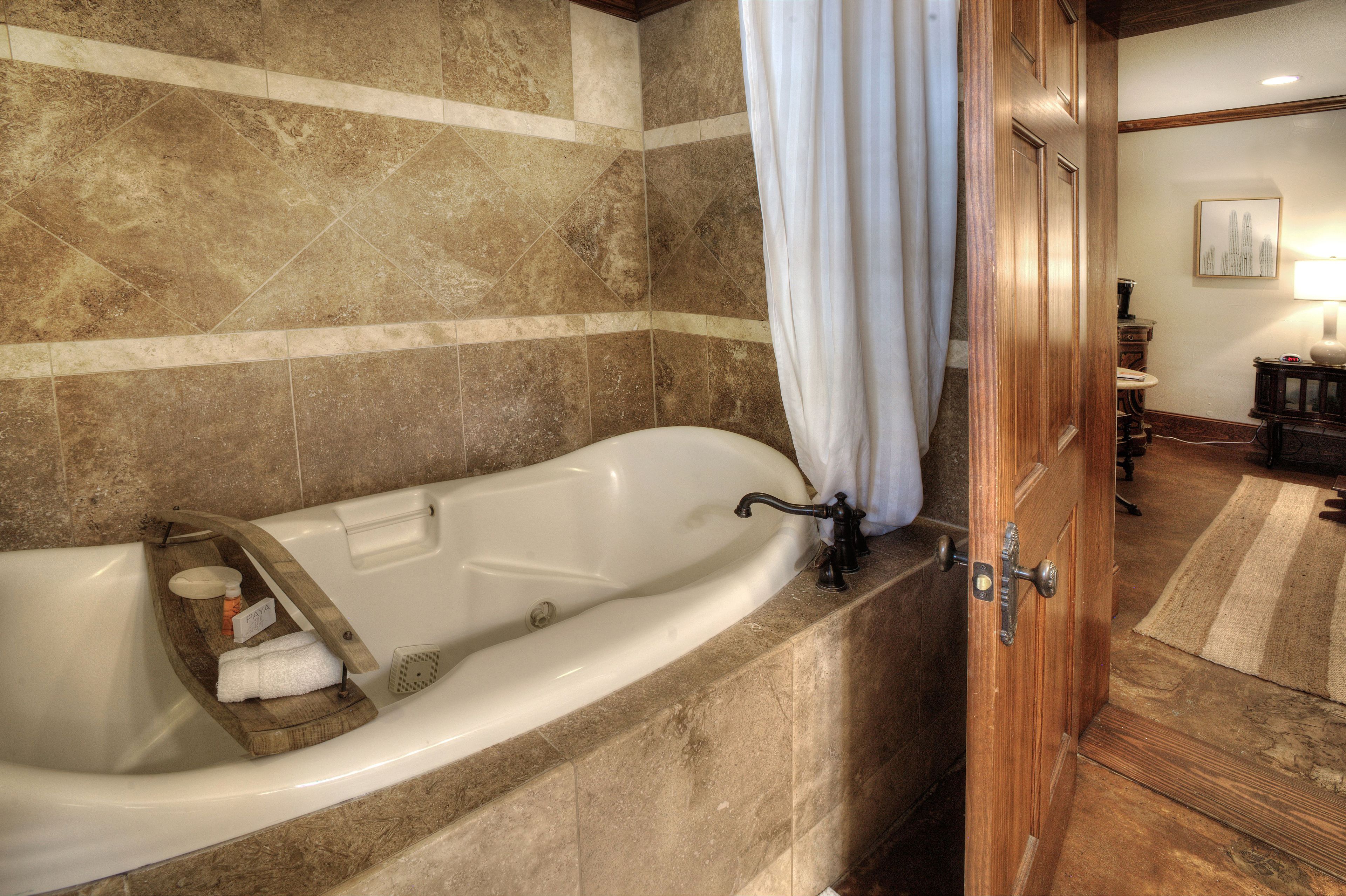 Un baño con una bañera independiente, una bandeja de madera con artículos de tocador y una puerta de madera.
