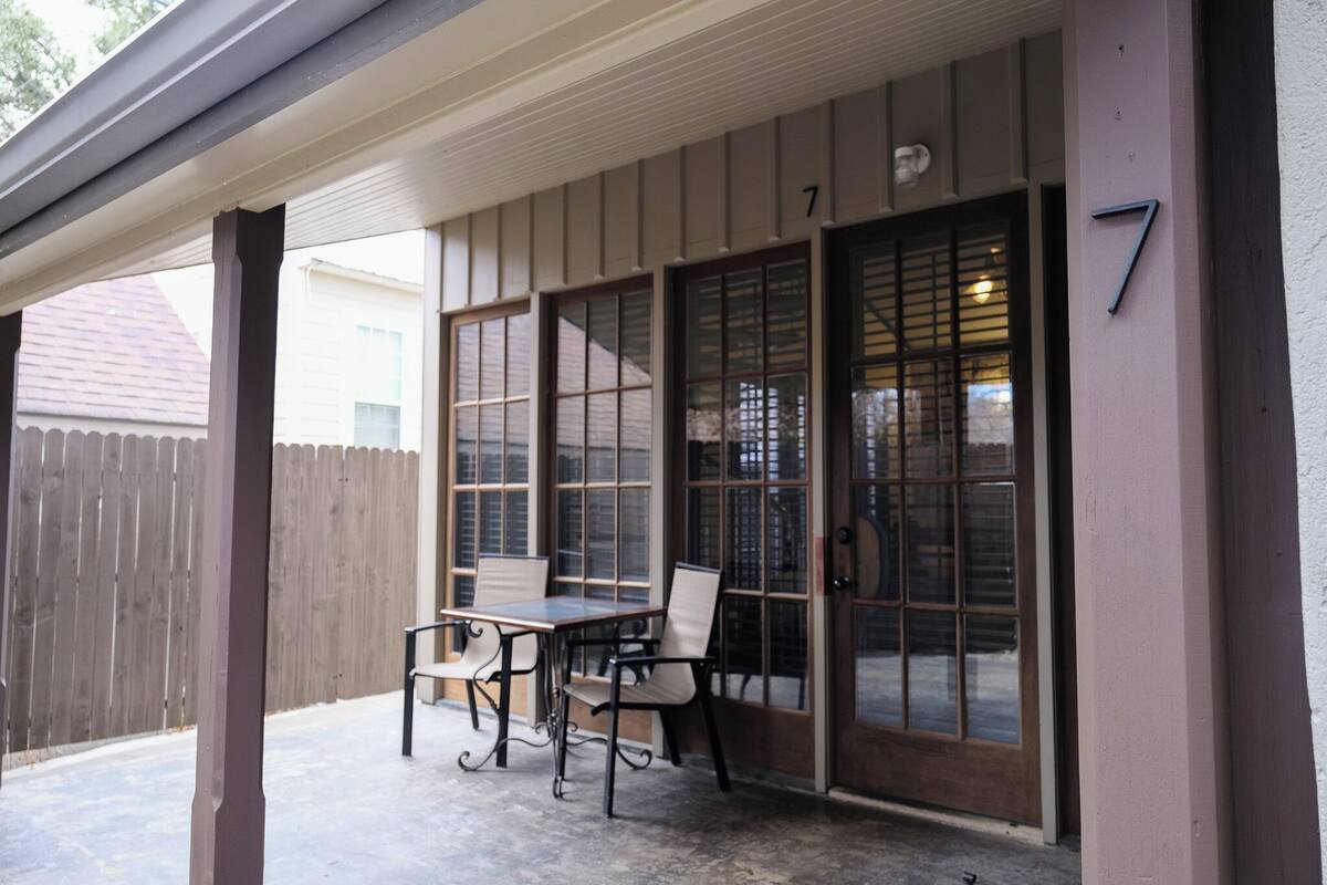 Une terrasse couverte avec une table et des chaises, une clôture en bois et le numéro de maison, qui est le 7.