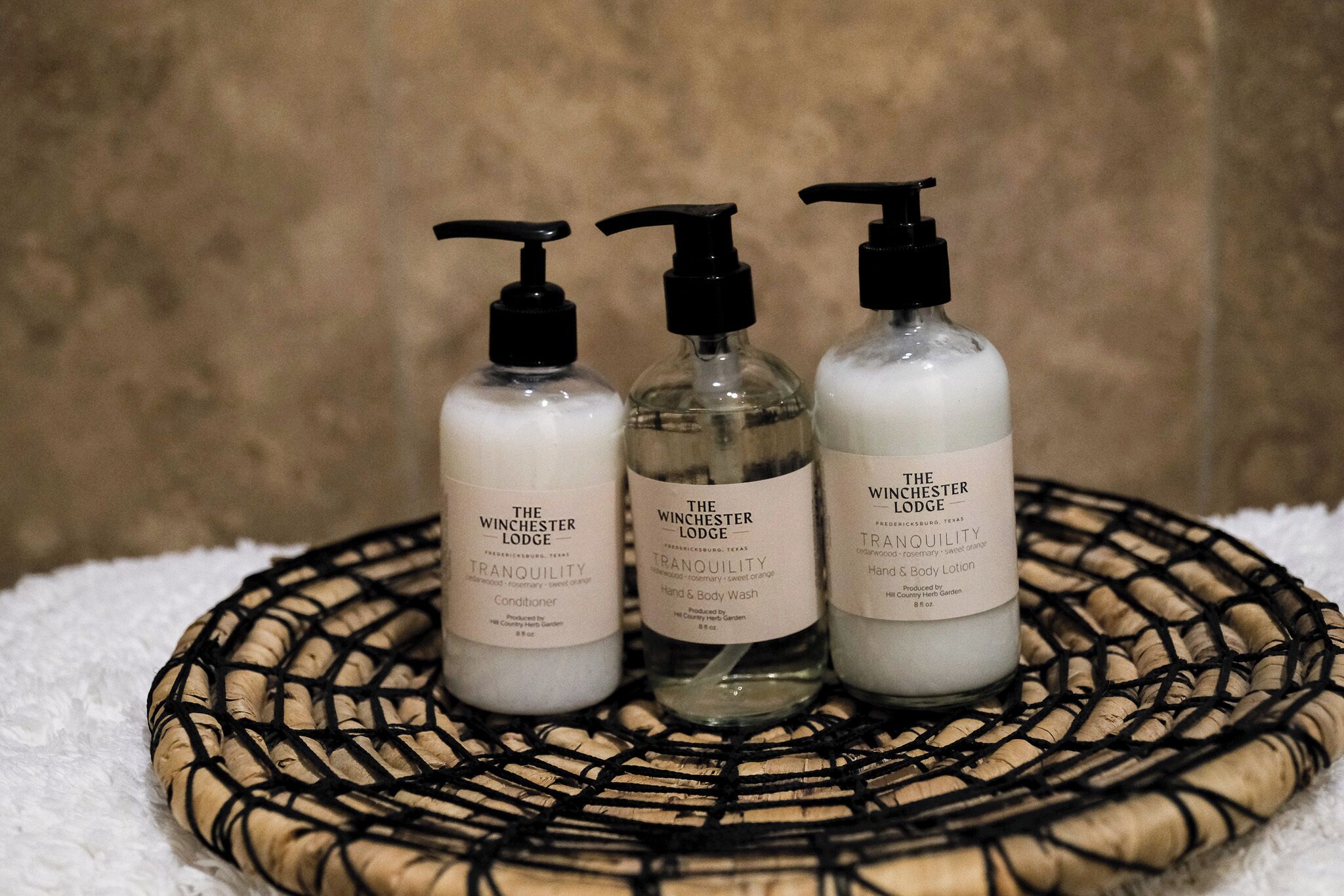 Tres botellas de productos de The Winchester Lodge sobre una bandeja tejida.