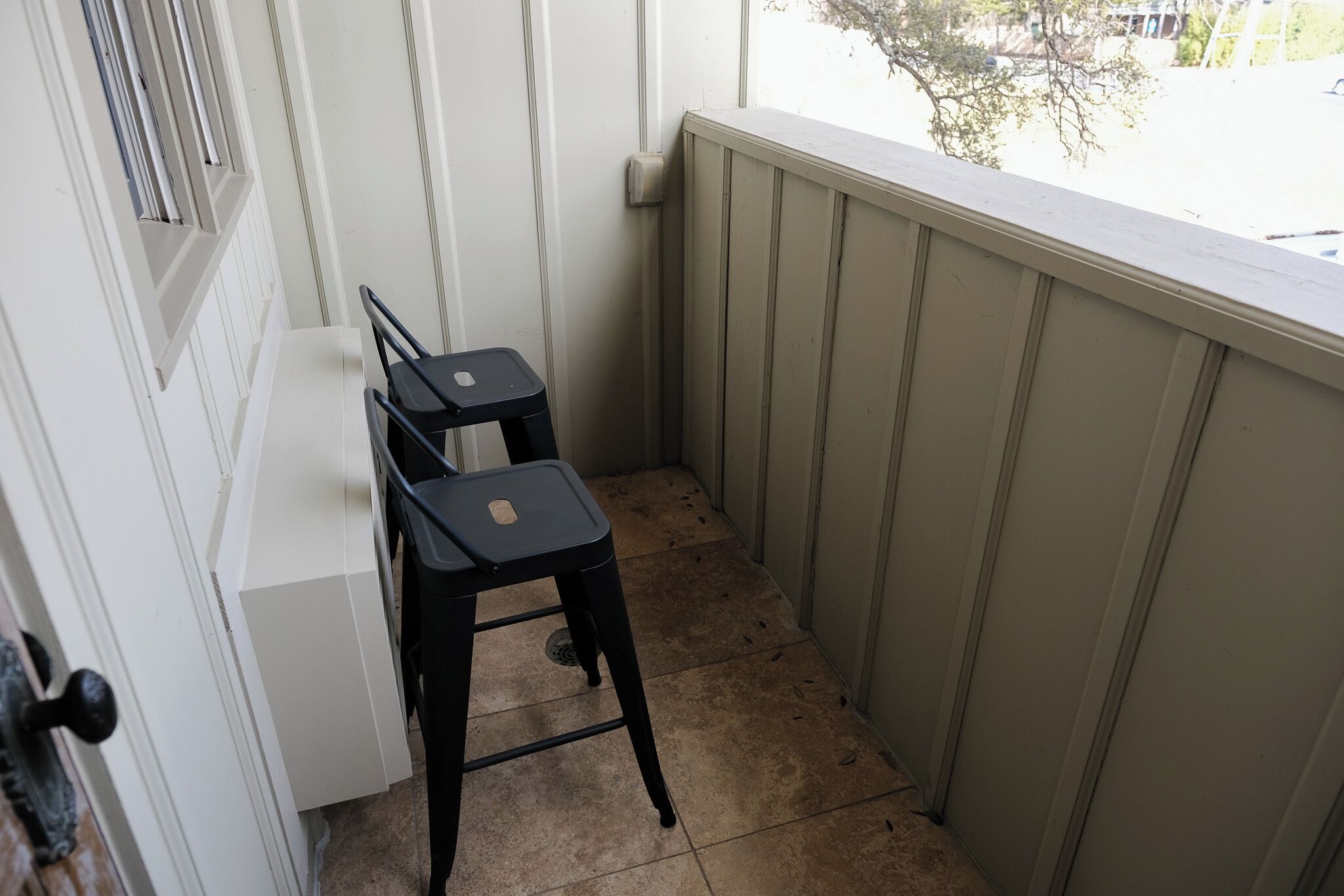 A small balcony with two black chairs and a white table.