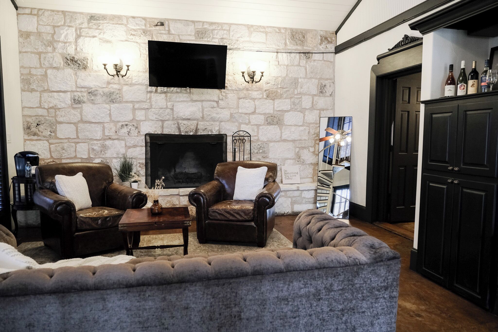 A cozy living room with a stone wall, a fireplace, leather armchairs, and a flat-screen TV.