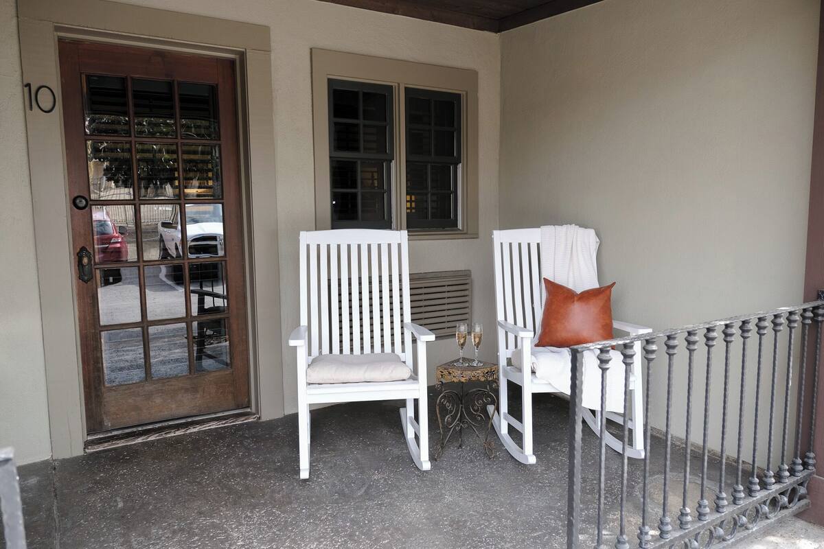 Une véranda avec deux fauteuils à bascule blancs, une petite table avec deux verres et une porte portant le numéro 10.