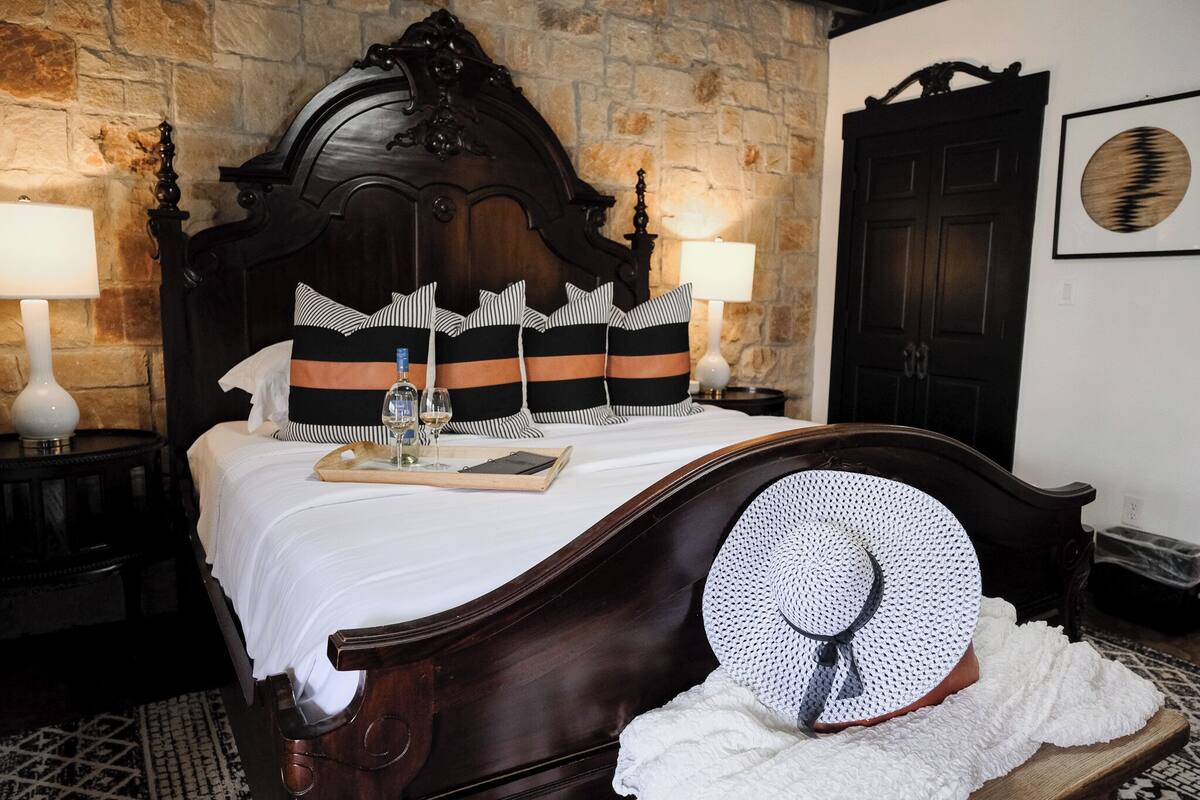 Une chambre à coucher avec un lit en bois, des coussins à rayures, une table de chevet avec une lampe et un tableau encadré au mur.