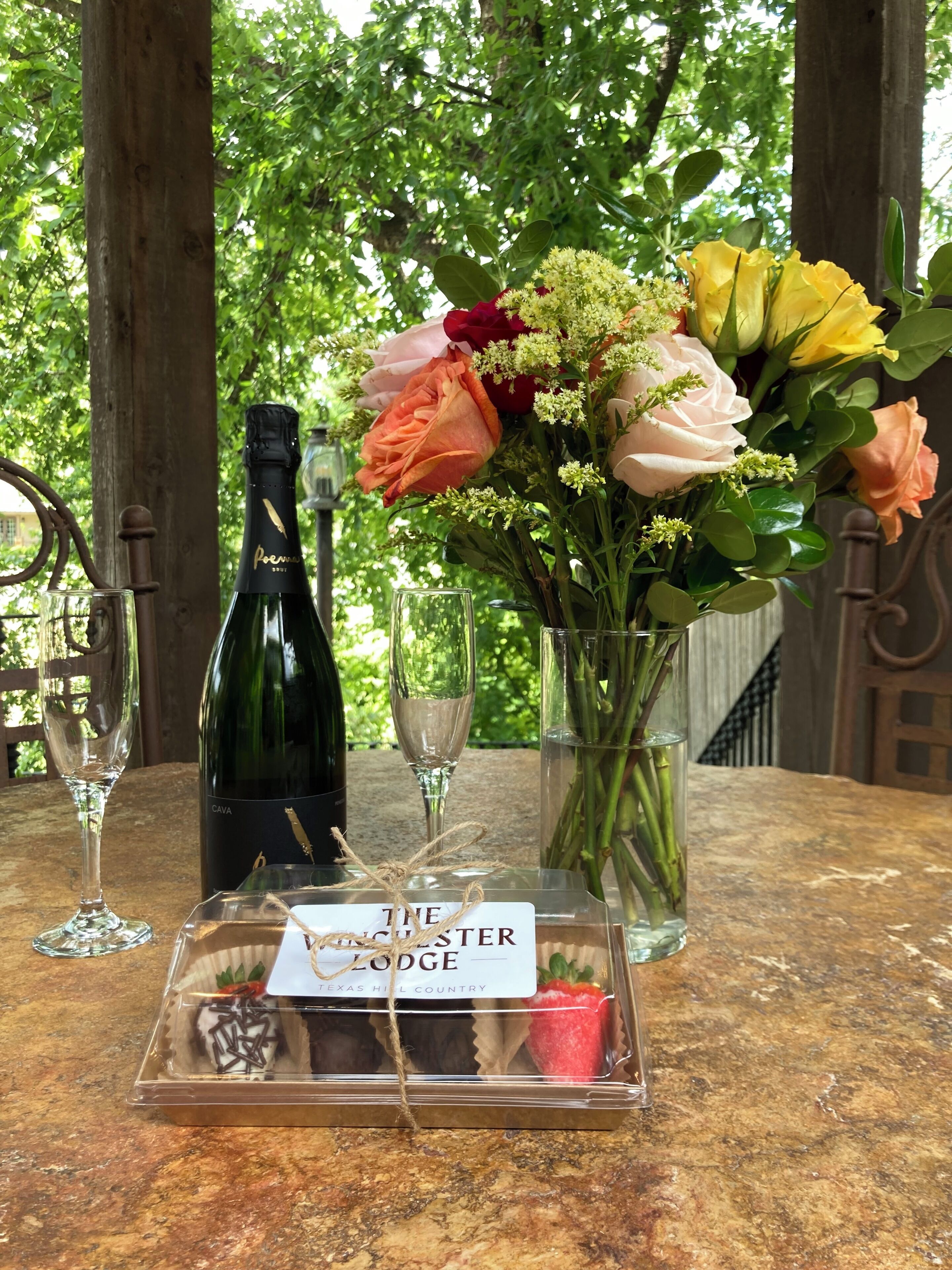 A table with a bottle of CAVA, a glass of wine, a bouquet of flowers, and a dessert tray labeled "The Ledge Lodge Texas Hill Country".