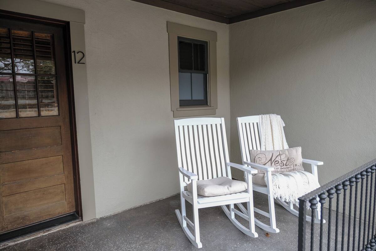 Une véranda avec une chaise berçante blanche et un banc, une porte en bois et une fenêtre au-dessus de la porte.