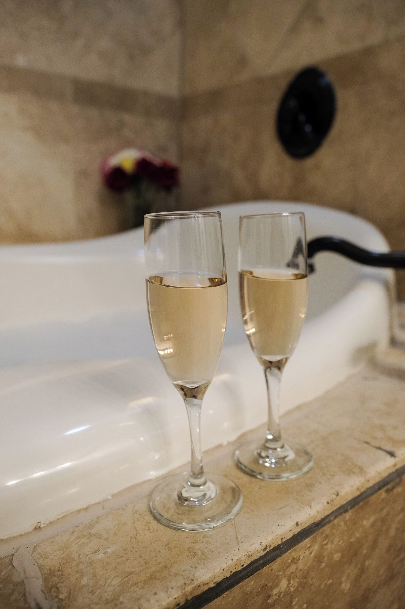 Dos copas de champán sobre una encimera de mármol, con una bañera al fondo.