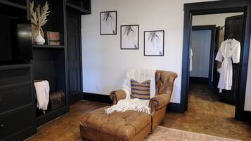 Een gezellige kamer met een bruine leren fauteuil, een witte plaid en een kamerbreed tapijt. Er hangen drie portretten van paarden aan de muur.