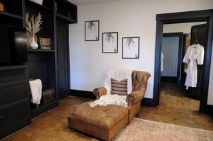 Een gezellige kamer met een bruine leren fauteuil, een witte plaid en een kamerbreed tapijt. Er hangen drie portretten van paarden aan de muur.
