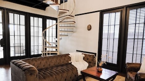 Una sala de estar moderna con un sofá marrón capitonado, una mesa de centro de madera y una escalera en espiral.
