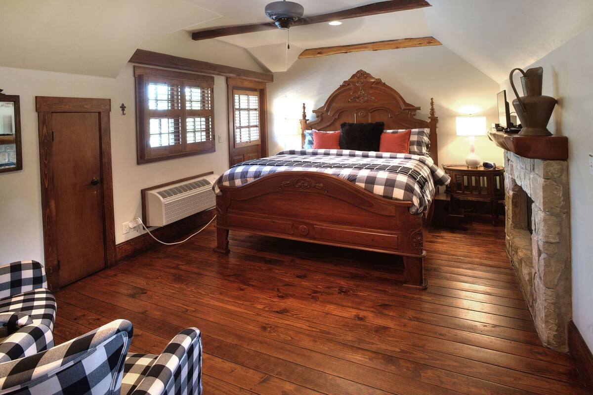 Une chambre à coucher avec un lit en bois, un ventilateur de plafond, une cheminée en pierre et une fenêtre avec des volets.