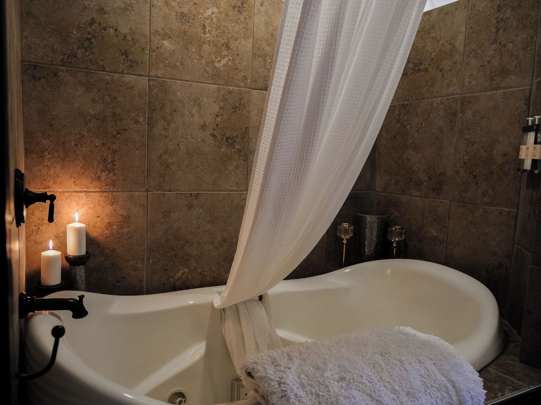 Ein Badezimmer mit einer Badewanne, zwei Kerzen, einem Handtuch und einer Duschkabine.