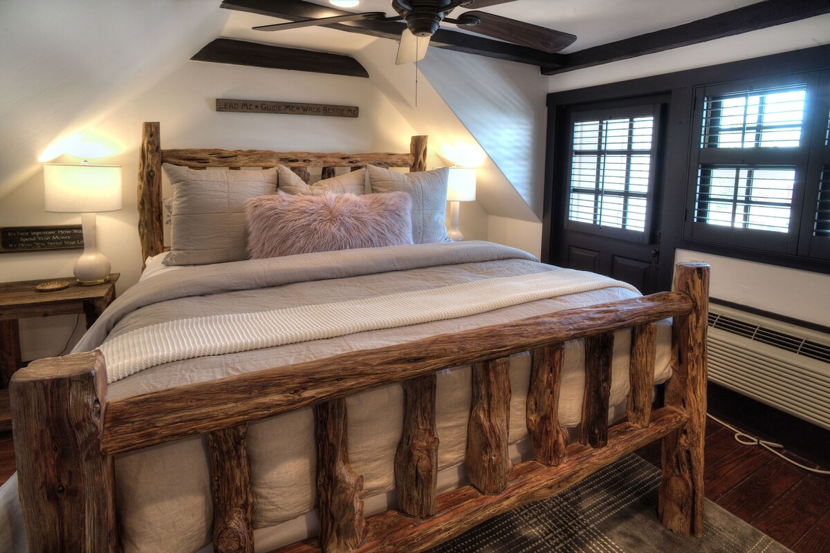Ein Schlafzimmer mit einem Bettgestell aus Holz, einer geneigten Decke und einem Fenster mit Jalousien.