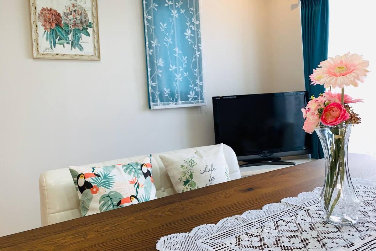 Una sala de estar con un sofá, una televisión, una mesa con mantel de encaje y un jarrón con flores.