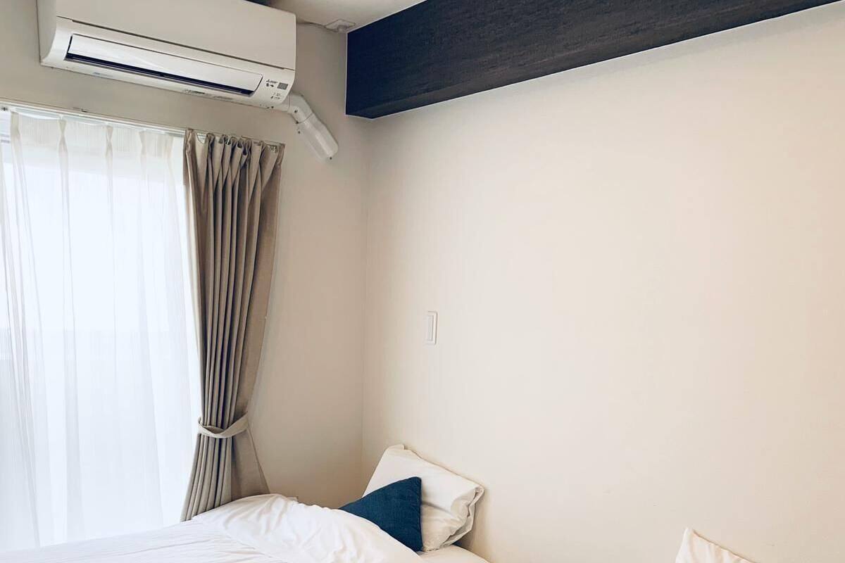Habitación de hotel con dos camas, una ventana con cortinas, un equipo de aire acondicionado y una pared decorativa oscura.