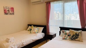 Ein Hotelzimmer mit zwei Betten, einem fensterbelaubten Fenster, einer Klimaanlage und einer Wanddekoration.