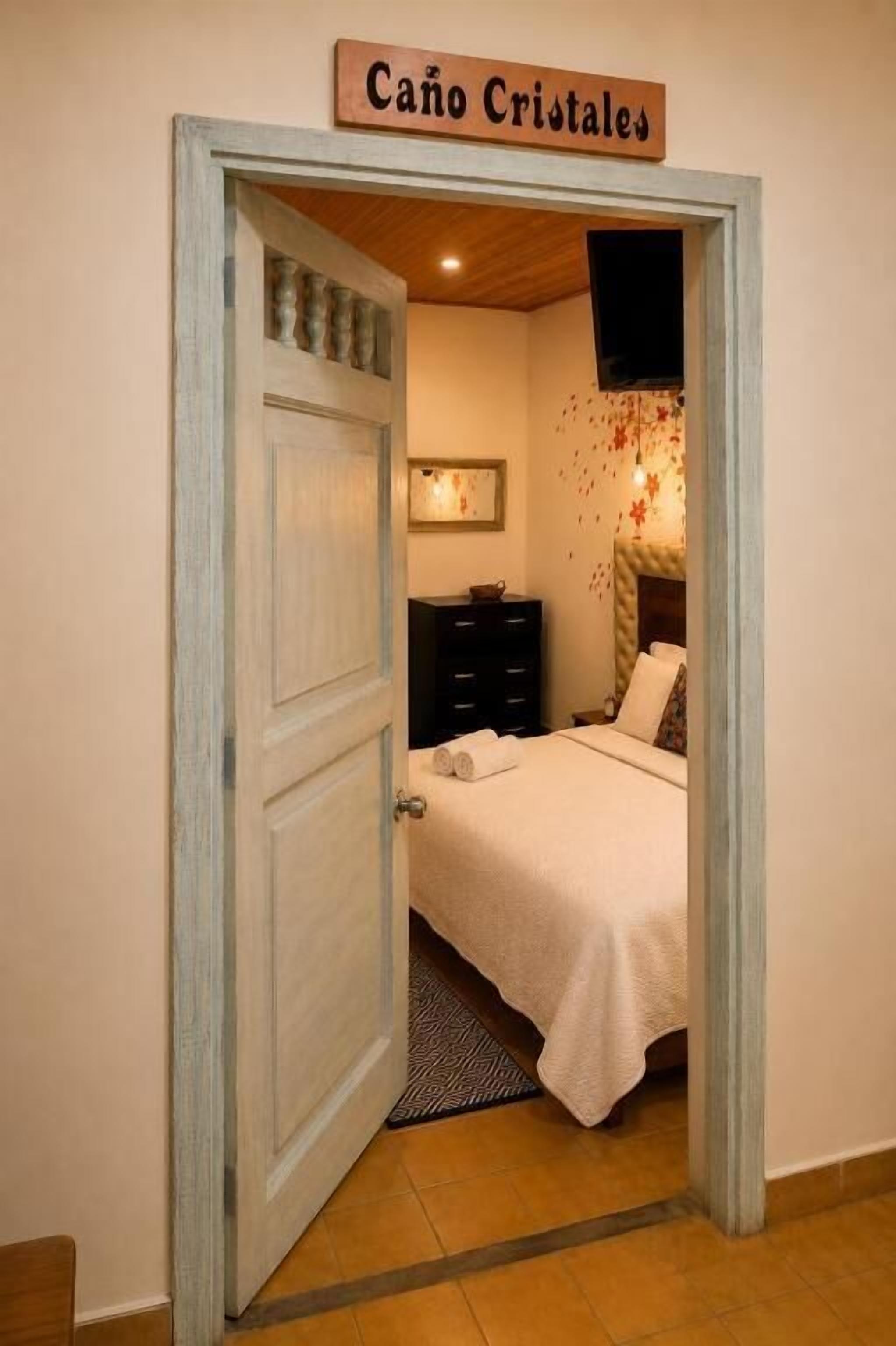 Un dormitorio con una cama, un aparador, un televisor y un cartel sobre la puerta que dice 'Cano Cristales'.
