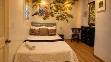 A neatly made bed with a quilted cover, a small bedside table with a lamp, and a chair.