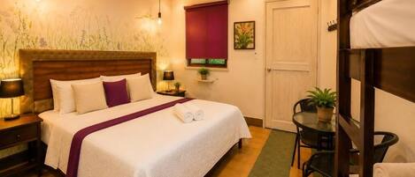 A neatly arranged bedroom with a bed, bedside tables, a small table with chairs, a door, and a window with a blind.