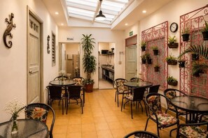 Un comedor con mesas y sillas redondas, una planta grande en maceta y un separador metálico decorativo con plantas.