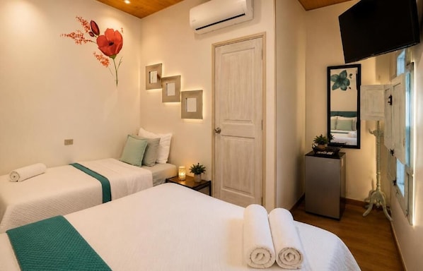 Habitación de hotel con dos camas, una puerta, aire acondicionado, televisión y un pequeño escritorio con lámpara.