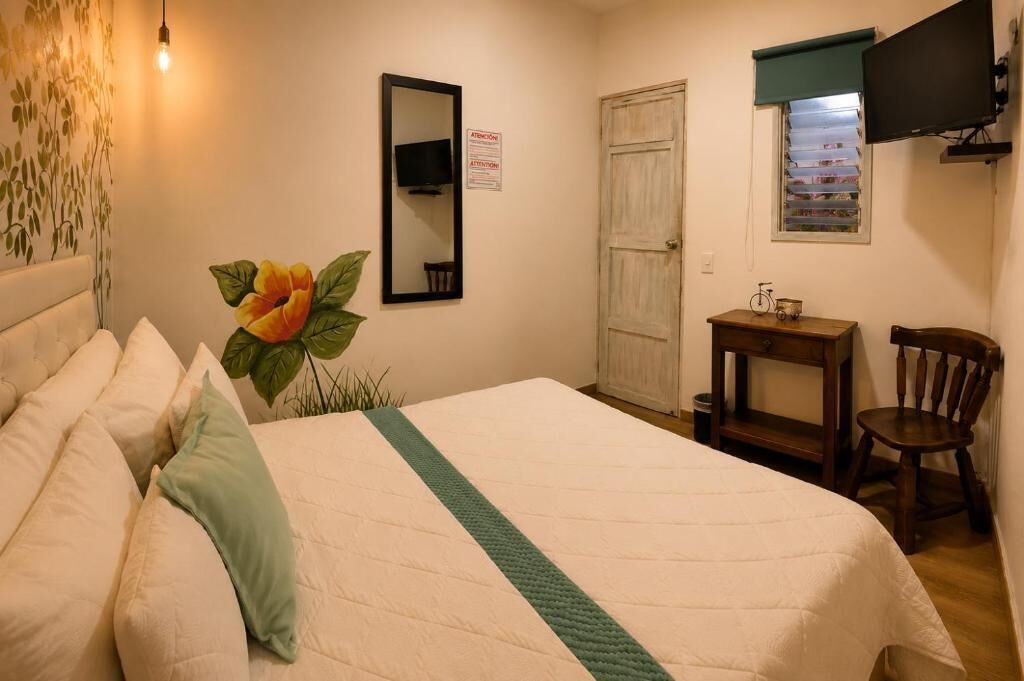 A bedroom with a bed, a mirror, a television, a door, and a small table with a chair.