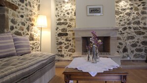 A cozy room with a stone wall, a fireplace, a sofa, and a table with a vase of flowers. - Roes apartments (Faistos)